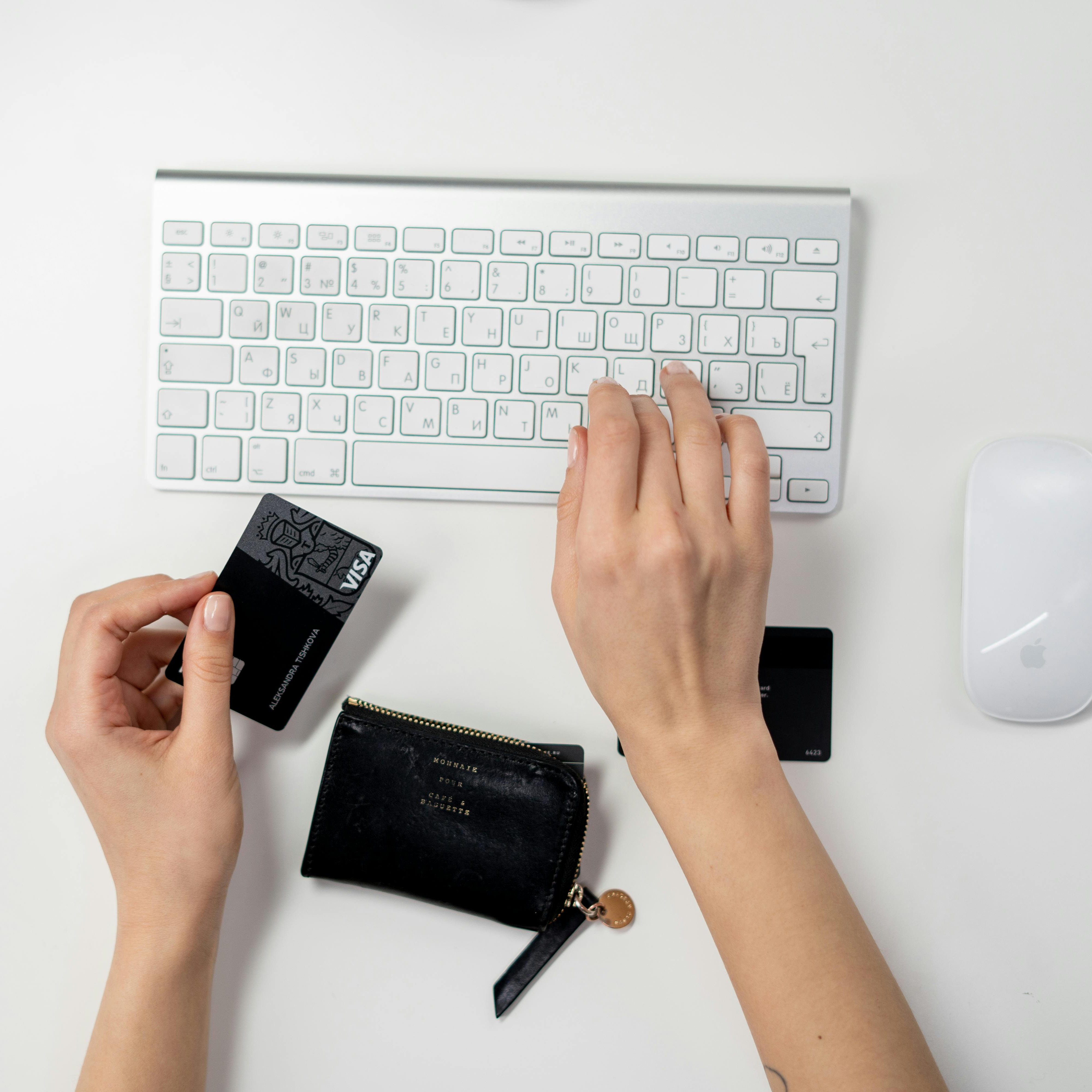 Symbolbild für Online-Einkauf. Linke Hand hält eine Visakarte und rechte Hand tippt auf einer silbernen Apple Tastatur.