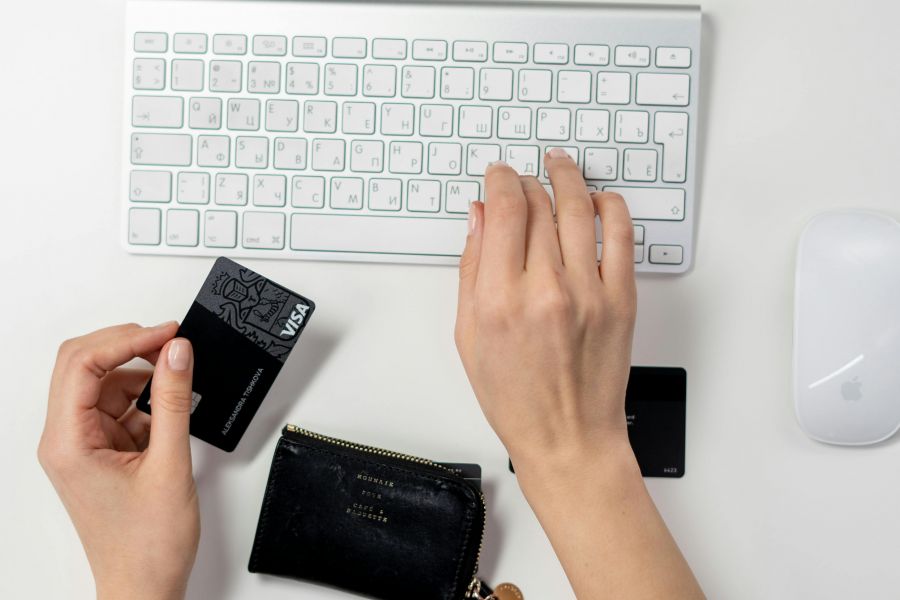 Symbolbild für Online-Einkauf. Linke Hand hält eine Visakarte und rechte Hand tippt auf einer silbernen Apple Tastatur.